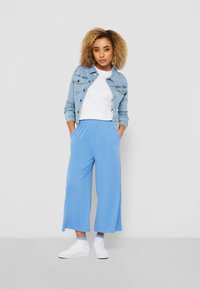 Pantalones de pierna ancha en azul claro con una cómoda cintura elástica, combinados con una camiseta blanca y una chaqueta de mezclilla. Zapatillas blancas completan el look.