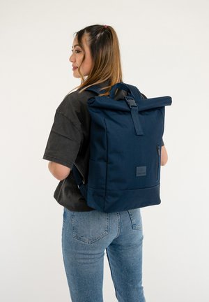 Navy roll-top backpack with adjustable straps, side pocket, and textured fabric. Features a logo patch on the front with a sleek, modern design.