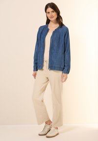 Jeansbombare i mörkblått, med dragkedja fram, elastiska manschetter och en avslappnad passform. Kombinerad med krämfärgade vida byxor och sneakers.