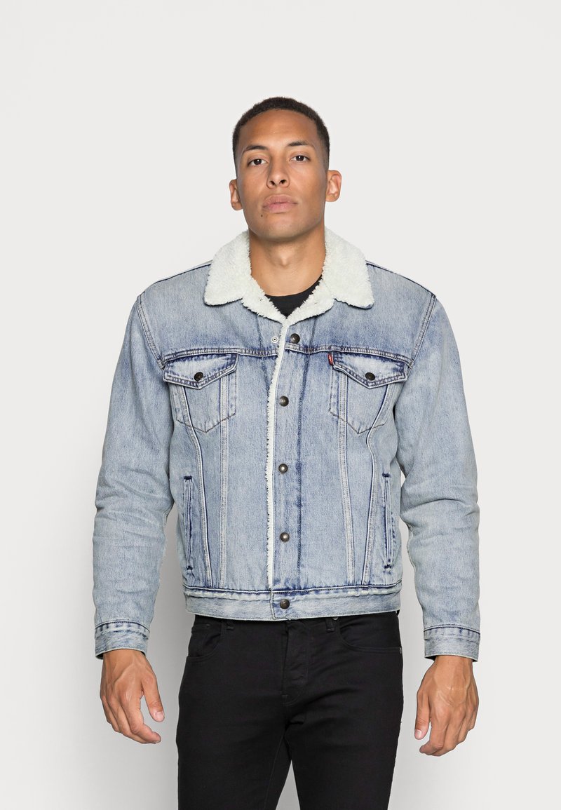 Giacca di jeans con un lavaggio azzurro chiaro, foderata in shearling bianco, caratterizzata da chiusure a bottoni, due tasche sul petto e cuciture distintive.