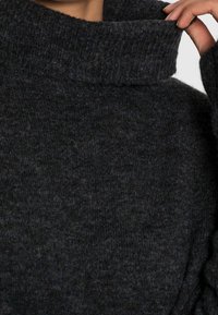 Mörkgrått stickat tröja med en tjock, ribbad hög krage och textil med struktur. Har långa ärmar och en avslappnad passform.