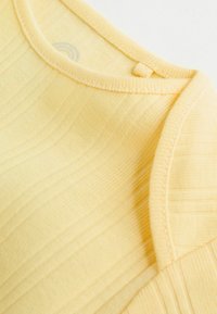 Dzeltena ribota tamborēta topiņa ar apaļu kakla izgriezumu, nelielu pogas detaļu un gludu tekstūru.