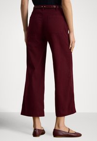 Bordo krāsas plašu kāju bikses no kokvilnas trikotāžas, ar jostasvietu, kurā ir cilpas jostai, aizmugurējām kabatām un gludu tekstūru.
