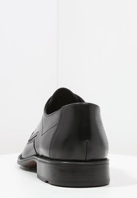 Chaussure en cuir noir avec une finition lisse, un bout légèrement arrondi, un petit talon et des détails de couture subtils sur le côté.