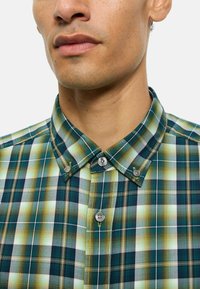 Kurzärmeliges kariertes Hemd in Grün, Blau und Weiß mit Knopf-umgelegtem Kragen. Verfügt über eine Mischung aus großen und kleinen Karomustern.