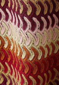 Tissu crocheté avec un motif zigzag ondulé dans des tons de rouge, jaune, rose, vert et orange, montrant des points ajourés détaillés.