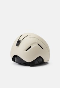 Matte-beige Helm mit aerodynamischem Design, ausgestattet mit Belüftungsöffnungen, einem verstellbaren schwarzen Riemen und einer strukturierten Rückseite.
