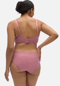 Sostenedor rosa y braguitas de cintura alta a juego, hechas de tela acanalada. El sujetador cuenta con tirantes ajustables y un cierre de tres ganchos.
