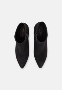 Ett par svarta mocka ankelstövlar med spetsiga tår och sidodragkedjor, sedda uppifrån på en vit bakgrund.