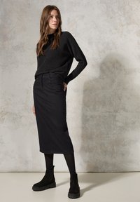 Falda larga negra con bolsillos frontales, combinada con un suéter negro texturizado y botas negras hasta el tobillo. Tejido suave con una silueta ajustada.