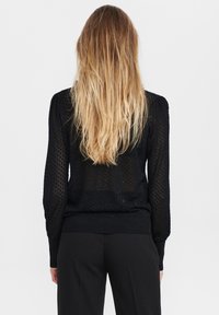 Musta neulepaita, jossa on tekstuuri kuvio, pitkät hihat ja resorireuna, yhdistetty mustiin housuihin, nähtynä takaa.