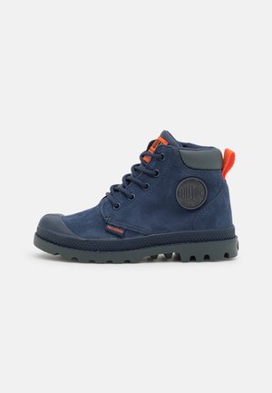 Bottine en daim bleu marine avec semelle noire, lacets noirs, languette orange et logo Palladium sur le côté et la languette.