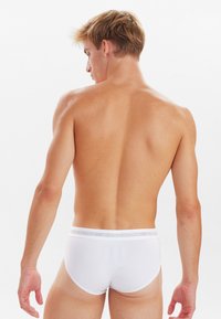 Hvide bomuldsunderbukser med elastisk talje, der viser mærkets logo. Glat tekstur, tætsiddende design og lavt skåret, synligt bagfra.