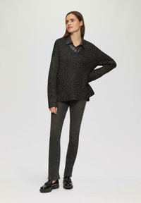 Ciemnoszary, oversize sweter z teksturowanej dzianiny z błyszczącymi nitkami, w połączeniu z dopasowanymi czarnymi spodniami i błyszczącymi czarnymi butami.