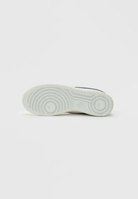 Potplat bijele Nike tenisice s uzorkom koncentrčnih krugova, vidljivim Nike logom, na jednostavnoj bijeloj pozadini.