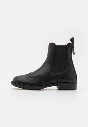 Black leather ankle boot with elastic side panel, brogue detailing on toe, and pull tab at the back on a white background.