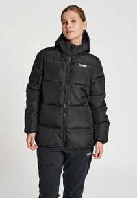 Zwarte pufferjack met een capuchon, voorzien van een rits aan de voorkant, elastische manchetten en een lichte glans; logo op de borst en onderrand.