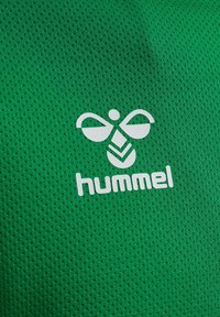Grøn sportsstof med et tekstureret mesh-mønster, med et hvidt stiliseret logo og mærkenavnet "hummel" trykt tydeligt.