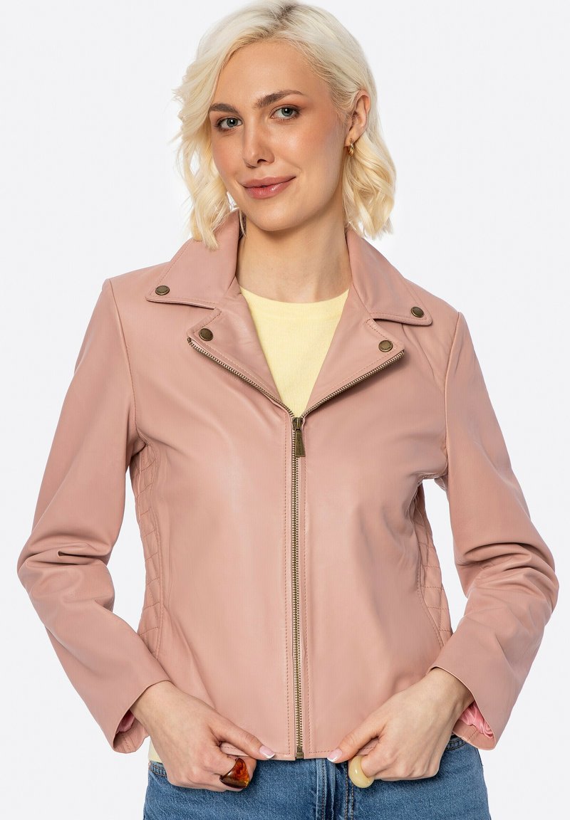 Giacca di pelle rosa con texture trapuntata, chiusura con zip e dettagli sul colletto a pressione. Il modello indossa una maglietta gialla, con le mani nelle tasche.