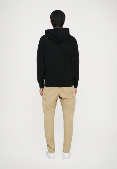 Sweatshirt preto com capuz, de corte simples e descontraído, combinado com calças cargo bejes claras com bolsos laterais e tênis brancos.