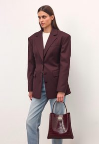 Burgundy oversized kavaj med spetsiga slag och en enskild bröstficka, ihop med ljusblå raka jeans och en glansig burgundyväska.