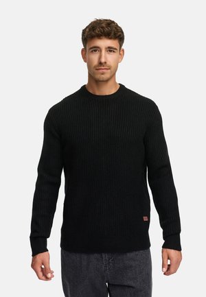 Maglione nero a coste con scollatura rotonda e maniche lunghe. Presenta una piccola etichetta del marchio in basso a sinistra. Abbinato a jeans.