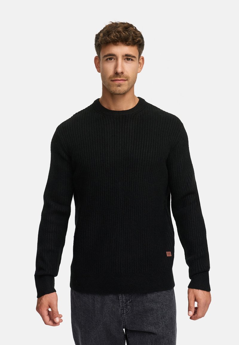 Suéter negro de punto acanalado con cuello redondo y mangas largas. Presenta una pequeña etiqueta de la marca en la parte inferior izquierda. Combinado con denim.