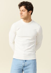 Maglione bianco a costine con maniche lunghe, dal collo rotondo e design aderente, abbinato a jeans azzurri, che mettono in risalto una trama morbida.