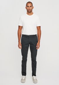 Pantalones negros ajustados de corte slim, hechos de una mezcla de algodón, combinados con una camiseta blanca de cuello redondo y zapatillas grises. Fondo neutro.
