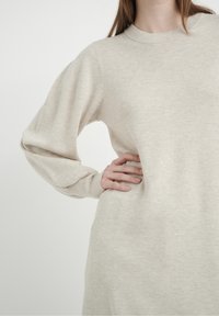 Pull-over beige clair avec une finition texturée, manches longues et encolure ronde, avec une coupe ample et des poignets côtelés.