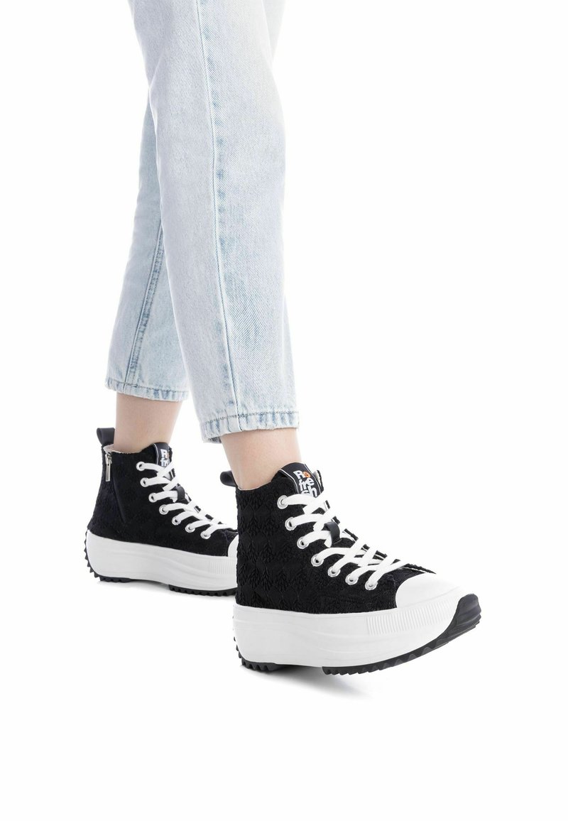 Zapatillas altas negras con suelas blancas, de tela texturizada y cierre de cordones. Presentan una cremallera lateral y un logo en la lengüeta.