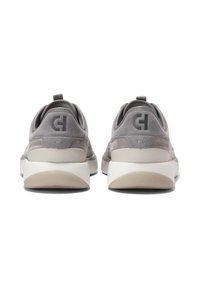 Pár šedých semišových tenisek s bílými podrážkami zobrazených ze zadní strany, s poutkem na patě a tmavým logem na podpatku.