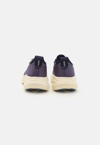 Baskets de sport violettes avec une tige en tissu texturé, un col rembourré et une semelle rembourrée de couleur crème avec un logo subtil sur le talon.