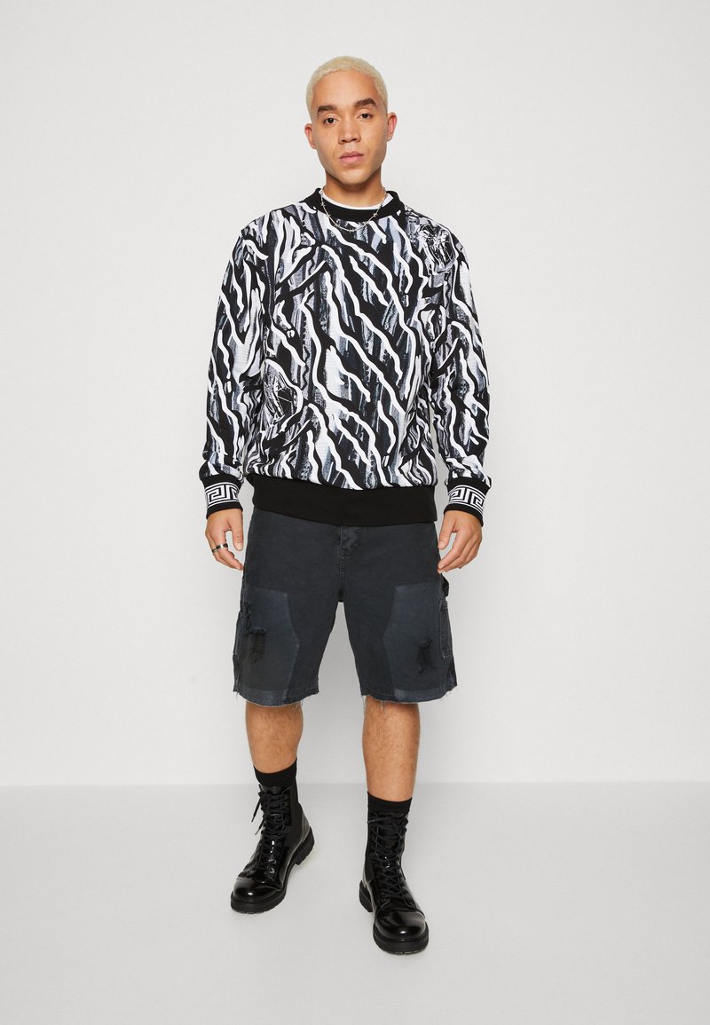 Svart og hvitt langermet sweatshirt med abstrakt mønster, kombinert med knelengde mørke cargoshorts og svarte kampstøvler.