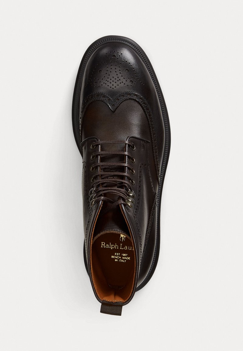 Bota brogue de cuero marrón con detalles perforados, diseño de cordones y suela en contraste. El interior presenta una etiqueta de marca y un forro marrón.