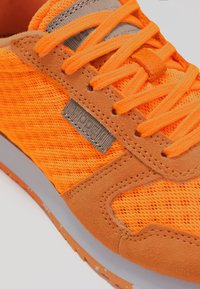 Ljusorange atletisk sko med nät- och mockamaterial, med grå accenter och platta snören, som visar en stilig och modern design.