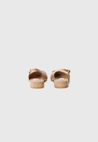 Sandales en cuir tanné avec une plateforme basse et un dos ouvert. Comprend une sangle sur le dessus avec un petit détail de boucle. Texture lisse.