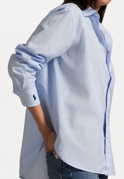 Chemise boutonnée bleu clair en coton avec une coupe décontractée, dotée de manches longues, d'un petit logo brodé sur le poignet et d'un ourlet arrondi.