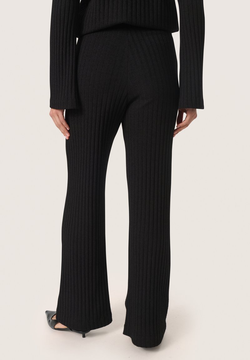Zwarte ribgebreide broek met een fitted taille en uitlopende benen. De stof is zacht en rekbaar, geschikt voor zowel casual als formele kleding.