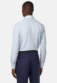 Camicia azzurra chiara con una texture liscia, maniche lunghe e colletto classico; abbinata a pantaloni scuri a righe verticali e una cintura nera.