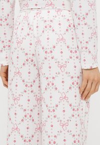Biela látka s kvetinovým vzorom obsahujúcim ružové ruže a mašle, textúrovaný povrch, elastický pás a voľný strih.