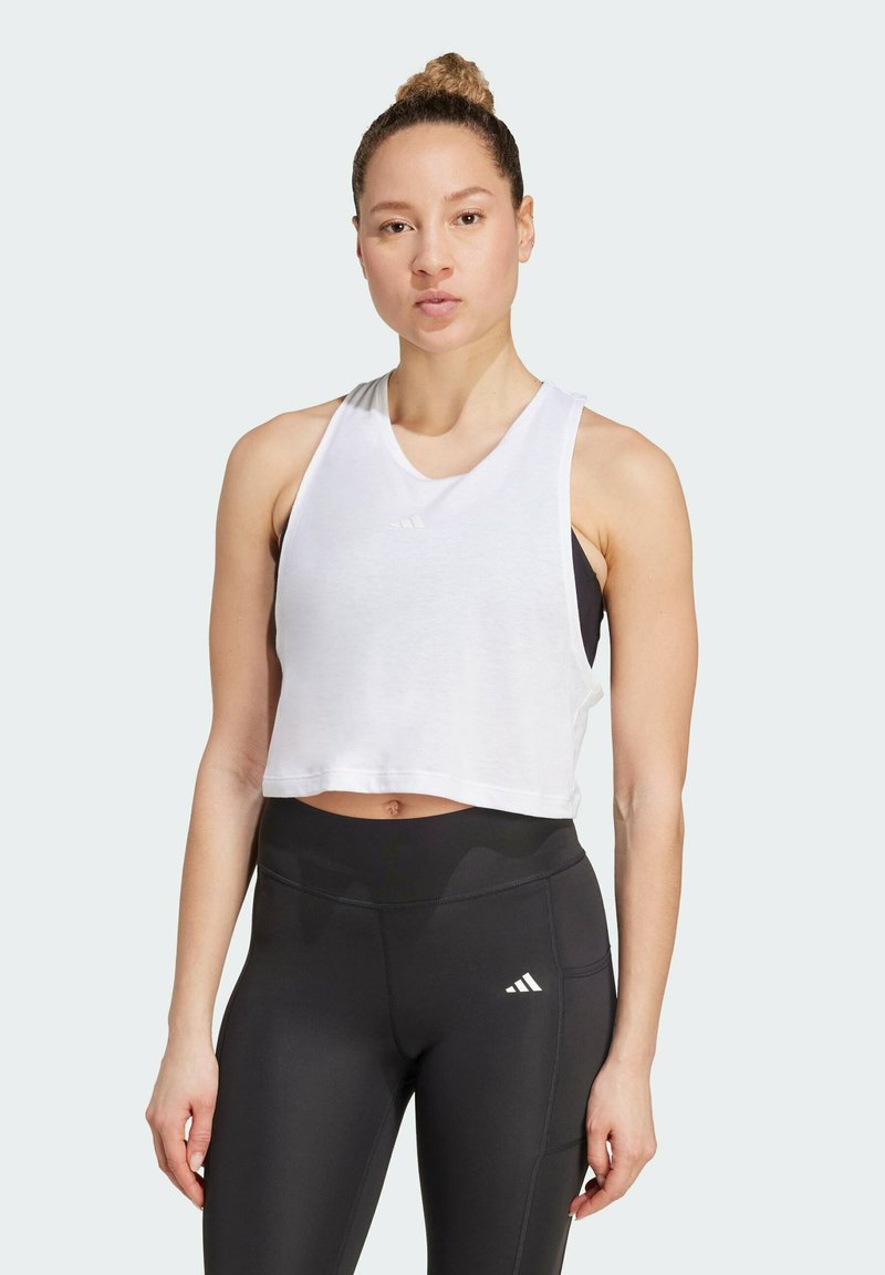 Crop top blanc avec un encolure dégagée, doté d'un logo subtil, associé à un legging noir taille haute, à la texture lisse et à la coupe ajustée.