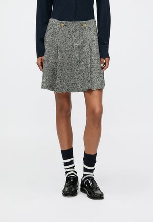 Szürke mintás pliszírozott szoknya aranygombos díszítéssel, párosítva tengerészkék zoknikkal, fehér csíkokkal és fekete lakkcipővel.