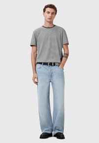 Gråstribet t-shirt med en sort krave, parret med lyseblå brede jeans. Iført med et sort bælte og kraftige sorte sko.