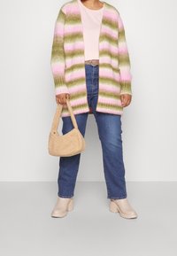 Cardigan tricoté avec des rayures roses, vertes et blanches ; porté avec un haut rose clair, un jean bleu, des bottines beiges à talons carrés et un sac à main pelucheux.