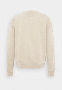 Béžová mikina z texturované, měkké látky. Má kulatý výstřih, dlouhé rukávy a žebrované manžety. Na zadní straně se nachází obdélníková visačka.