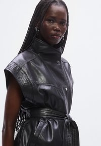 Zwarte leren jurk met een hoge kraag, korte mouwen, een getailleerde taille en knoopdetails aan de voorkant. Gladde textuur met stikaccenten.