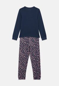 Tamsiai mėlyni ilgomis rankovėmis marškiniai derinami su tamsiai mėlynomis kelnėmis, kurių audinys puošia rožinė ir žalia leopardų rašto motyvus, išdėstyti ant baltos fono.