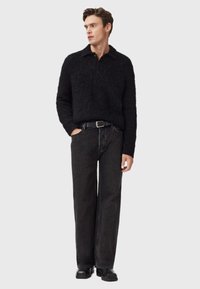 Suéter negro de terciopelo con cuello, combinado con jeans negros de corte holgado y zapatos negros. Diseño simple y casual con una apariencia texturada.