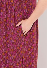 Lila Kleid mit pinken und orangenen Wellenmustern, das über eine Seitentasche verfügt. Der Stoff hat eine glatte Textur und fließt locker an der Taille.